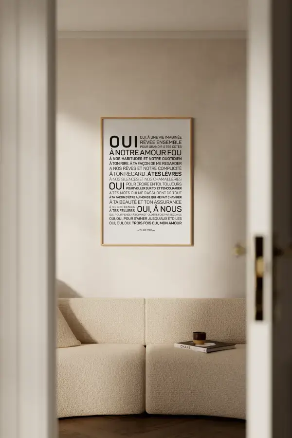 Un salon minimaliste comprend le canapé beige Mariage, une petite table et une affiche encadrée avec un texte français - une pièce de décoration élégante ou une idée cadeau - vue à travers une porte ouverte.
