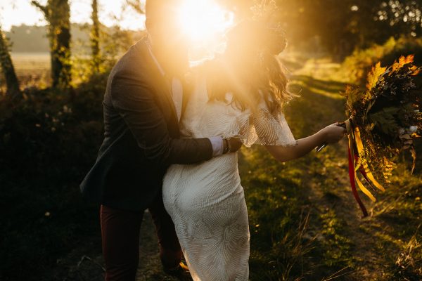 Une mariée et un marié s'embrassant dans un champ au coucher du soleil.