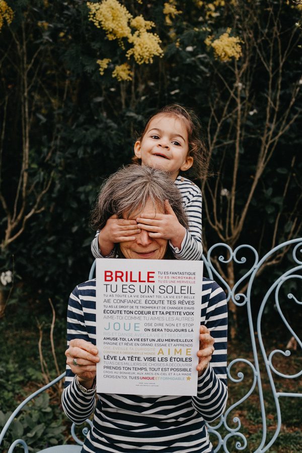 Une mère et sa fille brandissant une pancarte cadeau indiquant Brille, tu es un soleil.