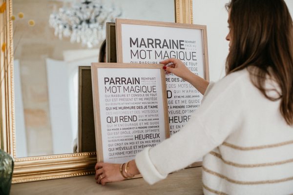 Une femme pose une affiche Parrain devant un miroir.