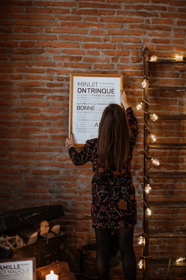 Une femme se tient à côté d’une échelle avec une affiche encadrée devant elle, tenant un Minuit, sur trinque.