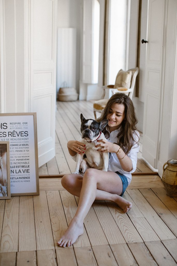 Une femme assise par terre avec un cadeau et un chien devant une affiche.