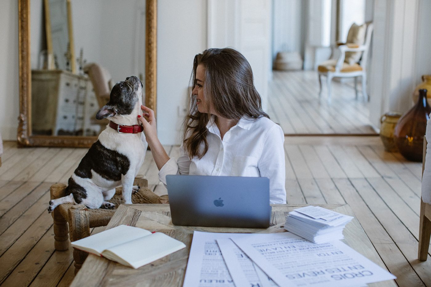 Une femme assise à un bureau avec un chien et un cadeau devant son ordinateur portable.