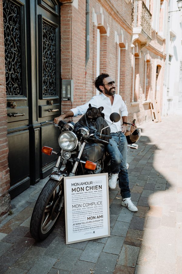 Un homme assis sur une moto à côté d’un panneau Chien.