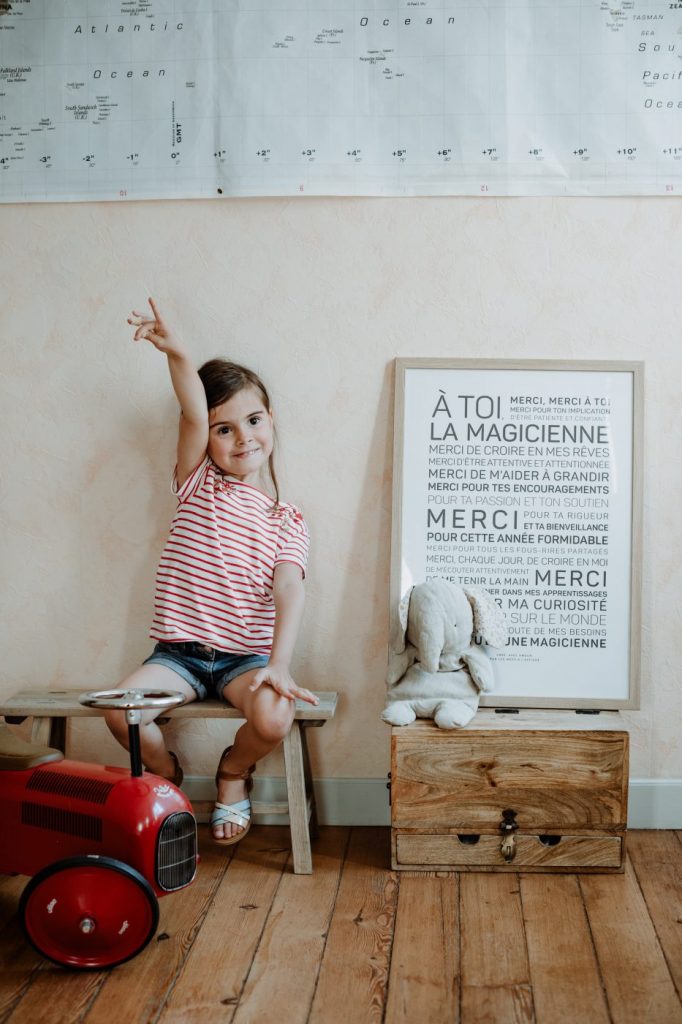 Une petite fille est assise sur un banc en bois à côté d'une affiche sur le thème "idée cadeau".