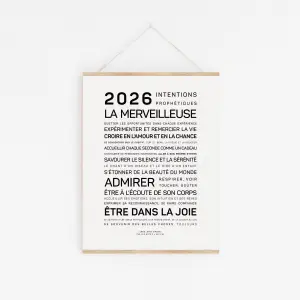 Une affiche minimaliste intitulée "2025, la merveilleuse" est accrochée à un mur blanc. Elle comporte une liste de phrases françaises inspirantes en texte noir.