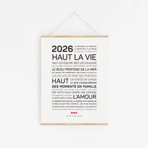 Une affiche minimaliste "2026, haut la vie" avec un texte en français sur le bonheur, l'amour et les souvenirs de famille en noir et blanc, affichée sur un mur dans un cadre en bois avec une ficelle.