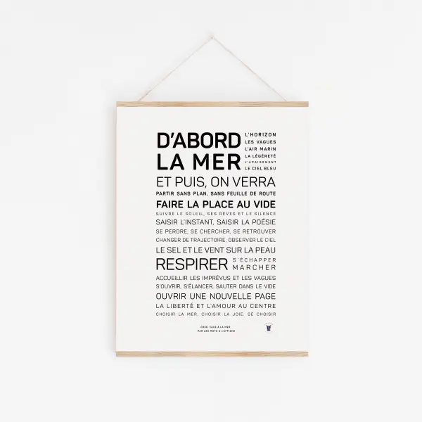 Une affiche française minimaliste intitulée « D'abord, la mer » présente un texte gras et régulier sur la mer et l'aventure. Elle est accrochée sur un mur blanc dans un cadre en bois avec une ficelle.