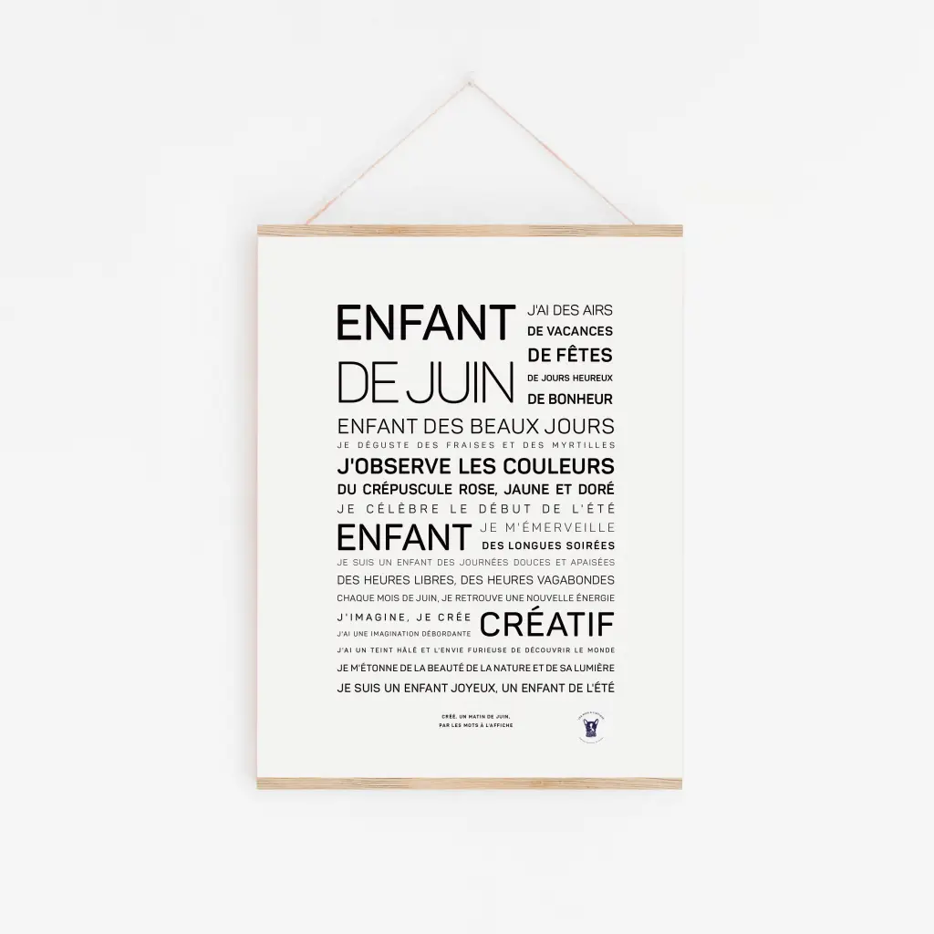 L'affiche Enfant de juin présente un texte français dans différentes tailles de police décrivant les qualités et les expériences d'un enfant de juin, imprimé sur du papier blanc et accroché au mur par une fine ficelle.
