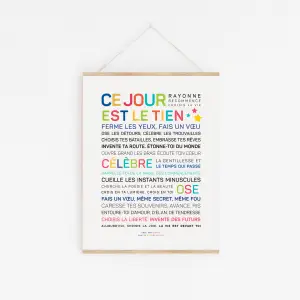 Une impression d'art encadrée intitulée "Ce jour est le tien !" présente des phrases de motivation multicolores en français sur le fait de vivre dans le présent et d'apprécier chaque moment, affichées sur un mur blanc.