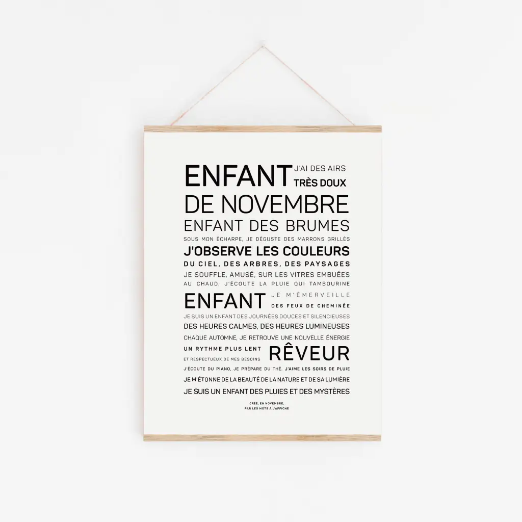Une affiche encadrée "Enfant d'août (Copie)" présente des textes en français dans différentes polices de caractères décrivant les traits de l'enfant d'août. Elle est affichée sur un mur blanc et suspendue par une ficelle.