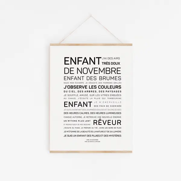 Une affiche encadrée "Enfant d'août (Copie)" présente des textes en français dans différentes polices de caractères décrivant les traits de l'enfant d'août. Elle est affichée sur un mur blanc et suspendue par une ficelle.