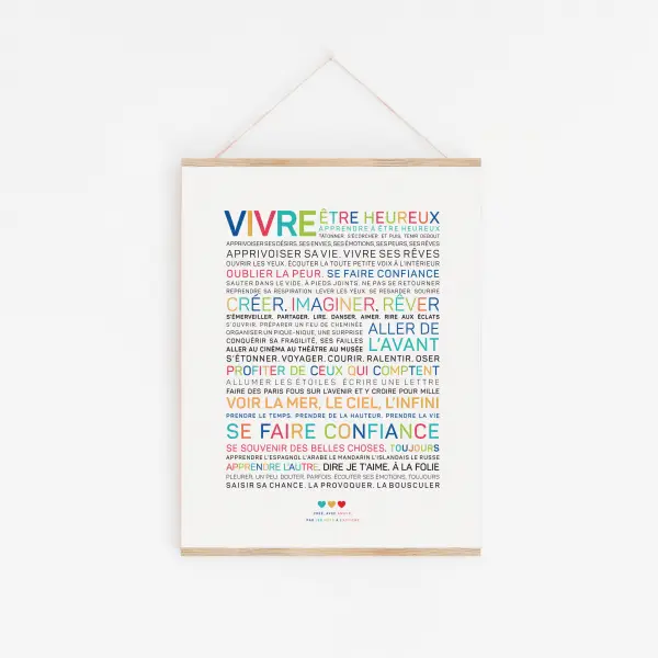 L'affiche "Vivre" est un design minimaliste avec des mots français colorés sur fond blanc, encadrés dans du bois clair et suspendus par une ficelle.