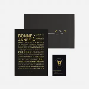Le set Letter press : Bonne année comprend une chemise noire avec fermeture par cordon, une carte de texte en français noir et or, ainsi qu'une petite carte illustrée d'un chat doré, le tout sur fond blanc.