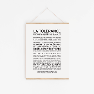 Une affiche intitulée "La tolérance - Voltaire" est accrochée à un mur blanc. Elle comporte un texte français en gras suivi de plusieurs lignes en lettres capitales noires.