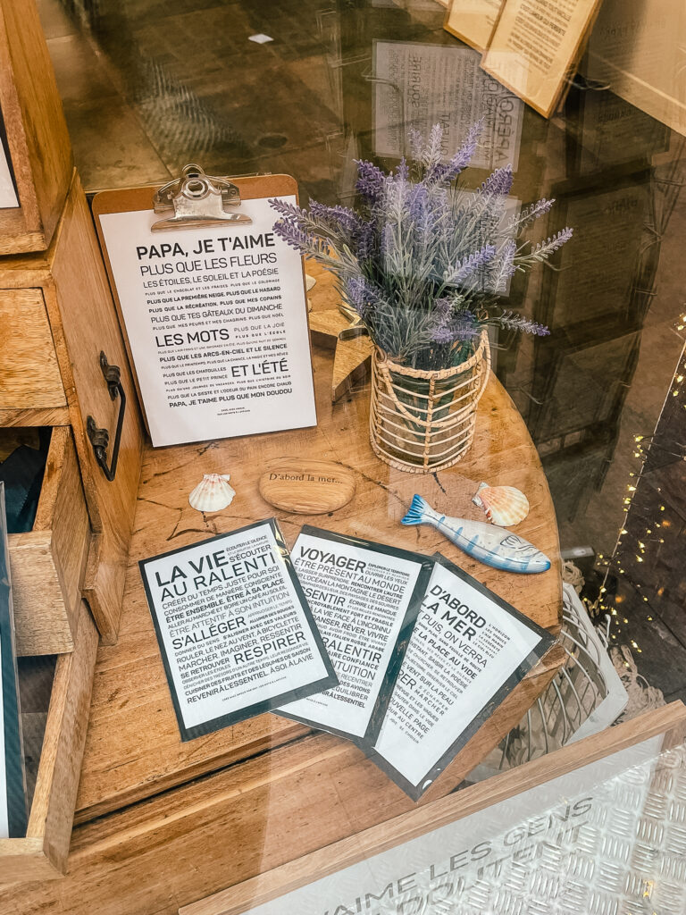 Présentoir en bois avec un bouquet de lavande dans un support en osier, une figurine de poisson et plusieurs cartes portant des citations en français, disposés sur une table en bois incurvée près d'une fenêtre.