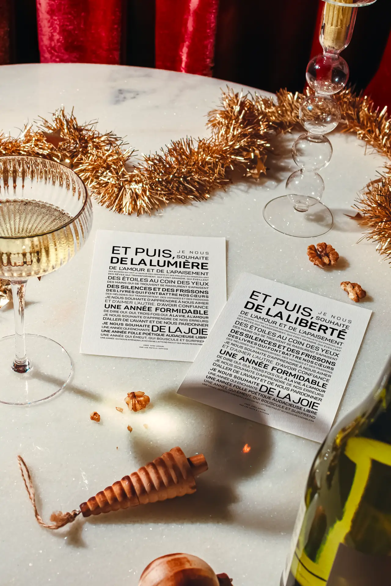 Deux verres de vin blanc, des décorations de fête et deux cartes imprimées avec un texte en français, posées sur une table en marbre.