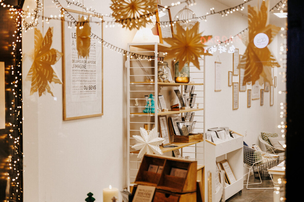 L'intérieur chaleureux d'une boutique, avec ses étagères remplies de livres et d'objets de décoration, éclairé par des guirlandes lumineuses aux couleurs chaudes et orné d'étoiles en papier suspendues.